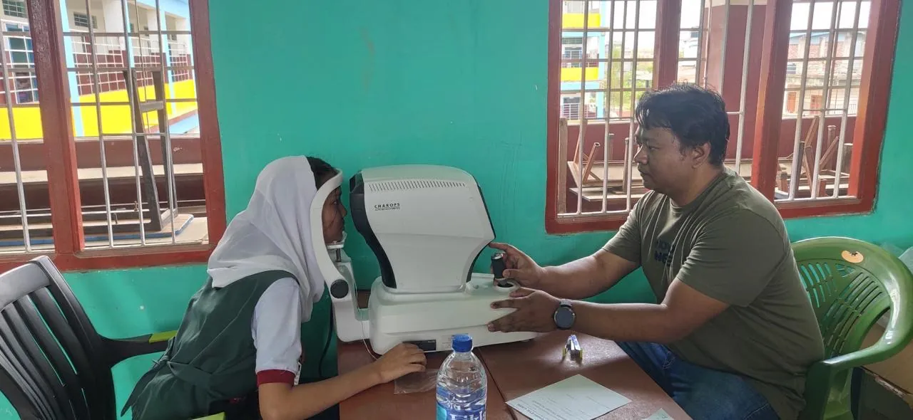 A student having her eyes measured on an autorefractometer at a school eye check-up workshop